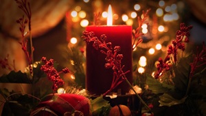 Rødt bloklys omgivet af røde grene og sløjfer og med gyldne lys i baggrunden