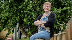 Smilende kvinde sidder på plankeværk i have