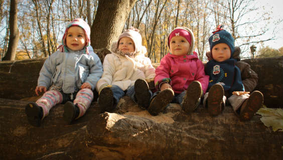 Fire små børn sidder på række i skovbund