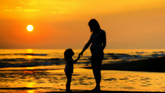 Silhuetter af en kvinde og et barn i en solnedgang ved vandet