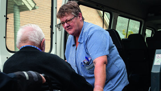 Sosu-assistent Ea Petersen hjælper ældre mand i kørestol ind i minibus