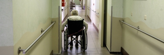 Ældre kvinde i kørestol på gang på plejehjem